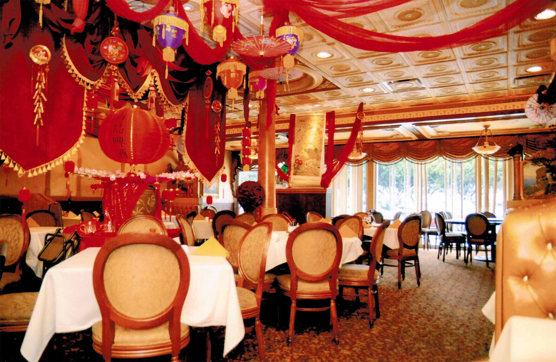 A dining room full of light and color. Intricate multicolored decor is shown hanging above tables draped with white tablecloths.